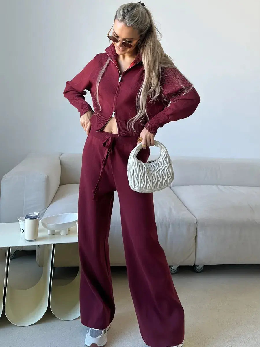 A white quilted handbag with a structured rounded shape and top handle paired with a women’s knit zip up cardigan and wide leg pant set.