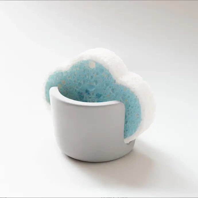 A light blue and white cloud-shaped sponge resting in a minimalist gray ceramic diatom mud sponge rack sink caddy holder.