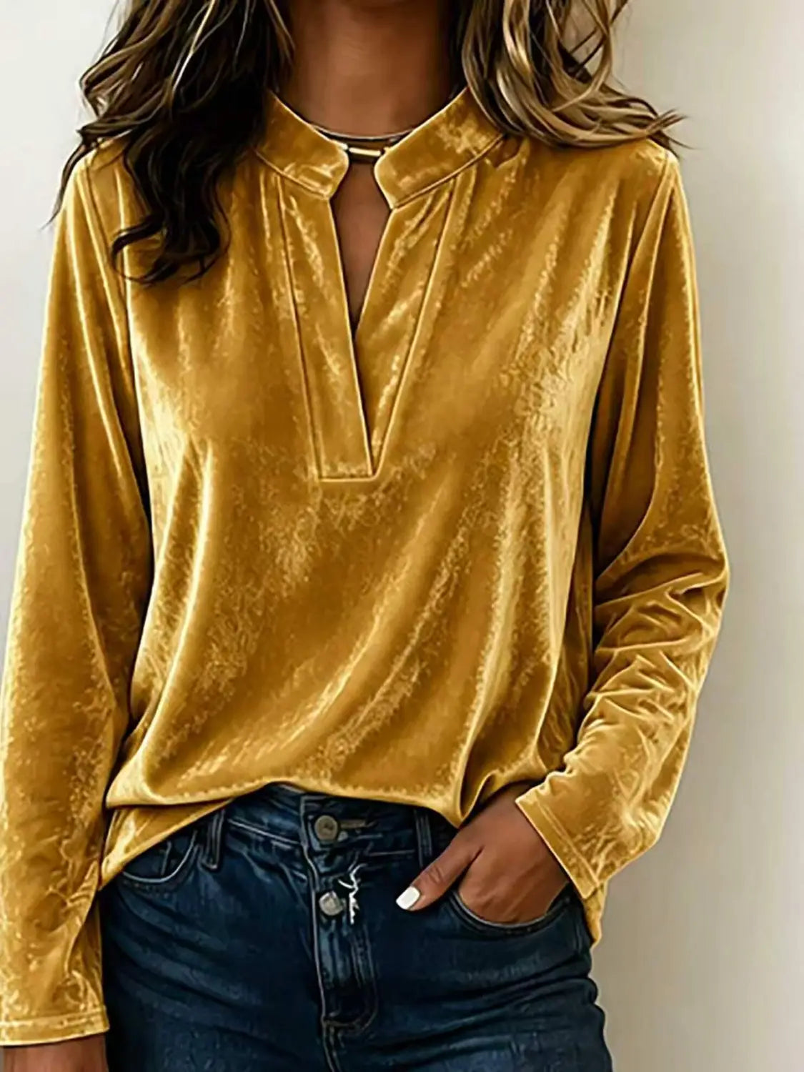 Eine goldgelbe Samtbluse mit V-Ausschnitt und langen Ärmeln für Damen aus einem weichen, strukturierten Stoff mit einem dezenten Muster.