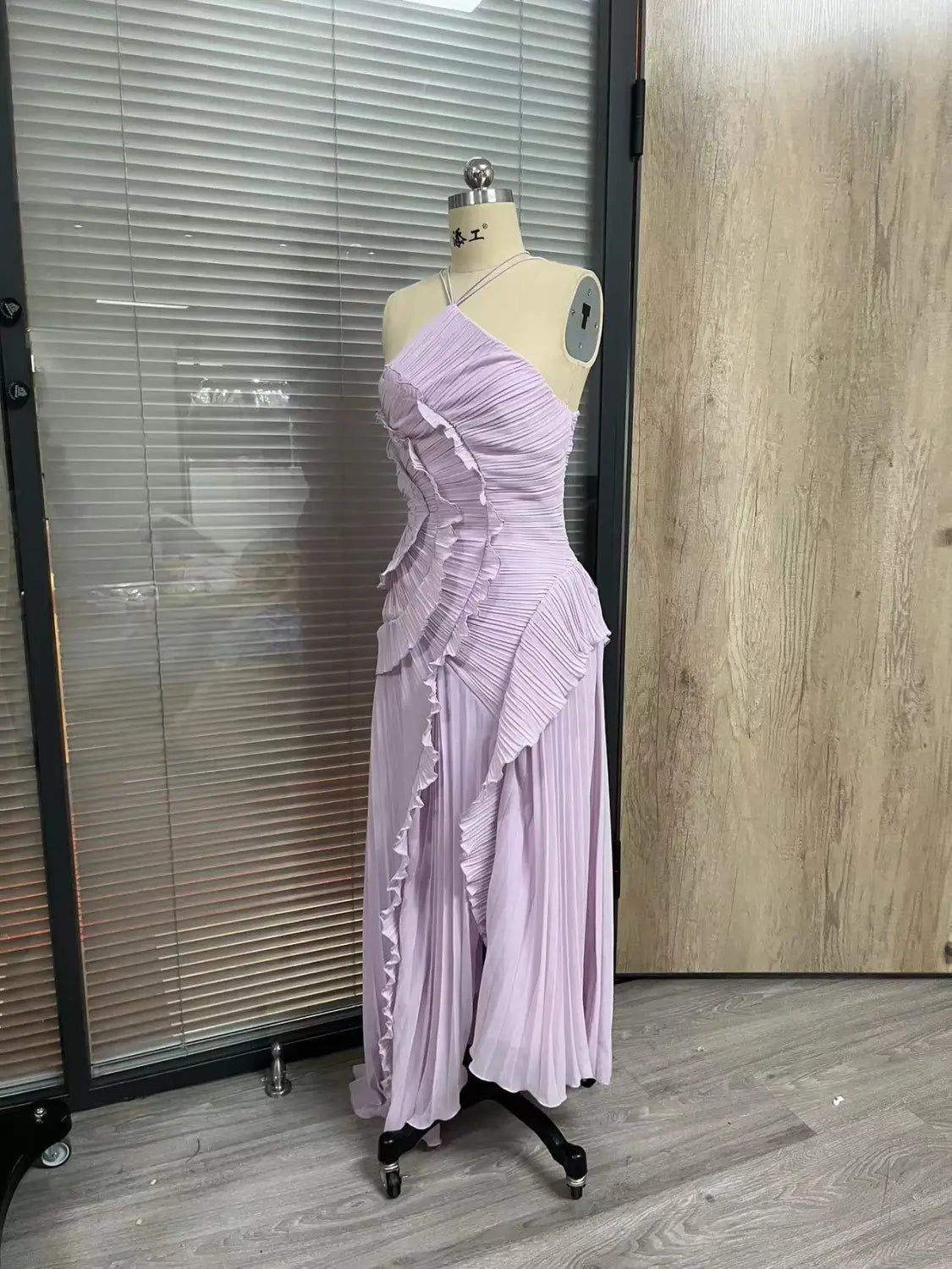 A lavender pleated chiffon maxi dress with asymmetrical ruffled detailing designed as a halterneck evening dress.