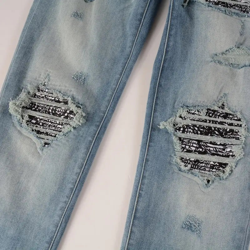 Men’s slim fit bandana patch light wash distressed jeans featuring ripped knee patches with black and white patterned fabric inserts.