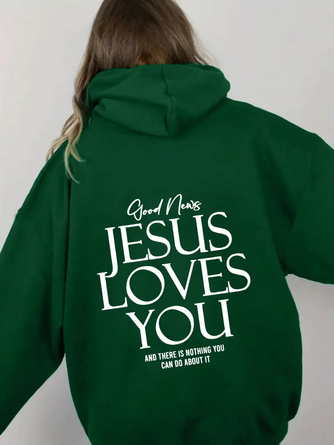 a dark green oversized streetwear kangaroo pocket hoodie featuring a bold white graphic that reads good news jesus loves you in large stylized letters