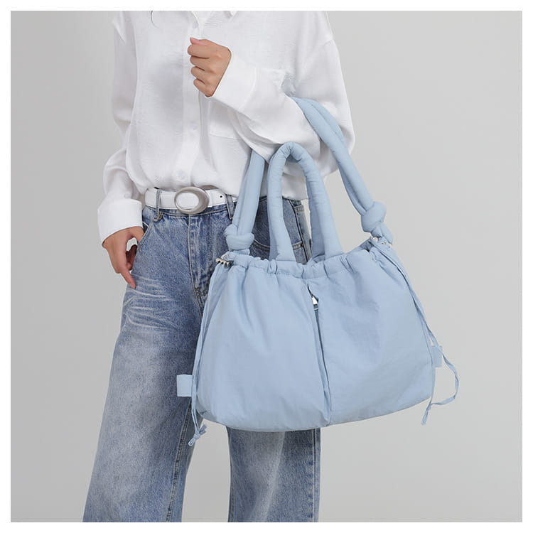 Light blue quilted puffer tote bag made of lightweight nylon with knotted handles and drawstring closure designed as a shoulder bag.