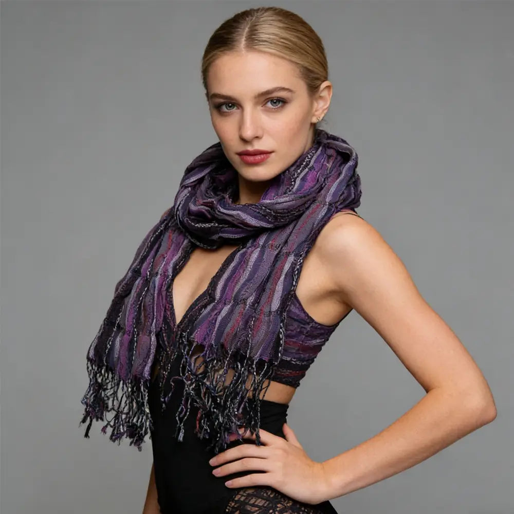 Une femme porte une écharpe froissée en jacquard violet, au tombé fluide, avec des motifs rayés subtils texturés et une frange sombre, en tant qu’accessoire d’hiver.