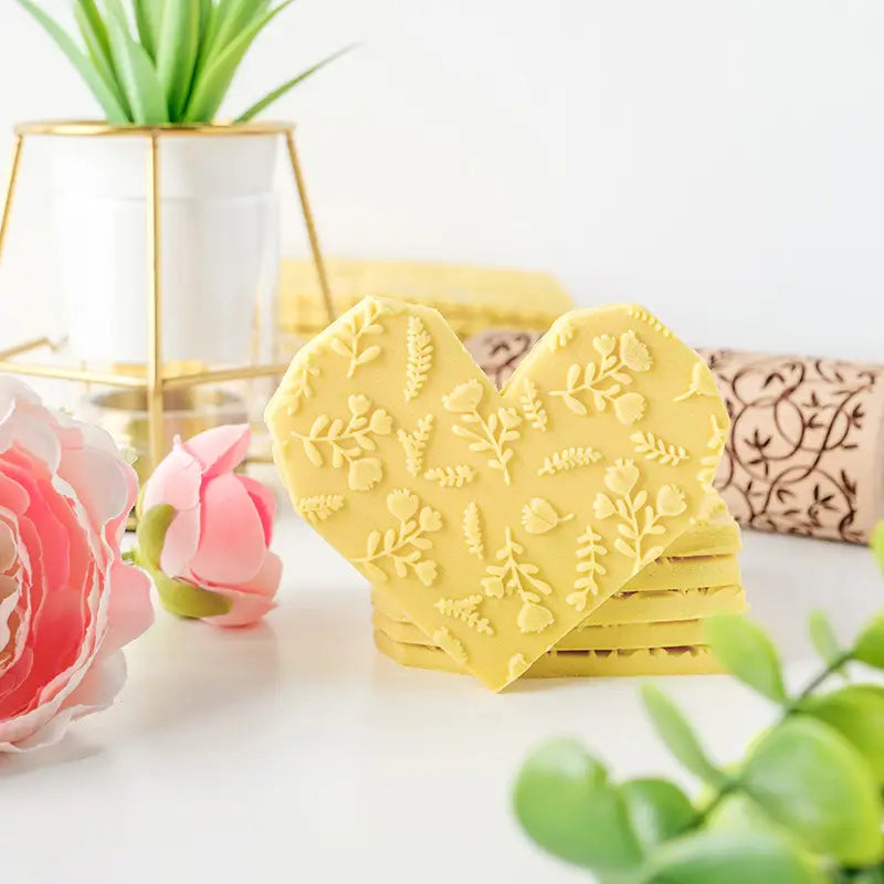 Dessous-de-verre en forme de cœur jaunes avec un motif floral en relief complétant un rouleau à pâtisserie en bois de hêtre en relief floral pour la cuisson.
