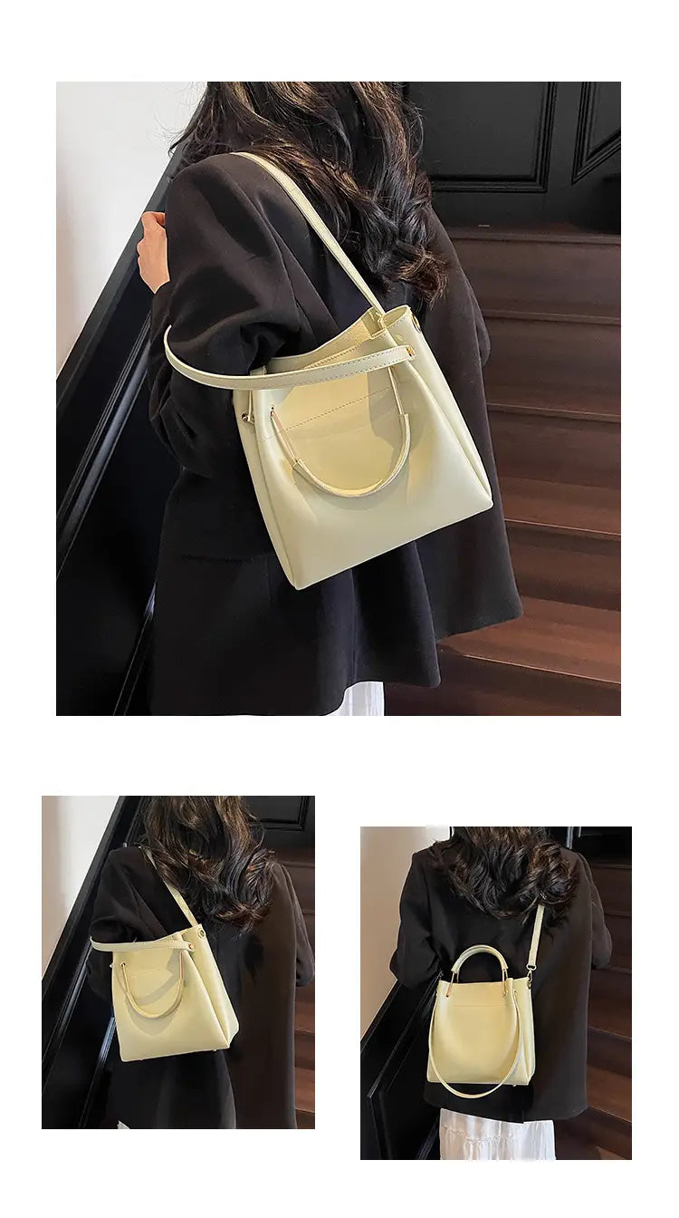 Cream-colored minimalist leather bucket bag with a top handle and detachable shoulder strap.