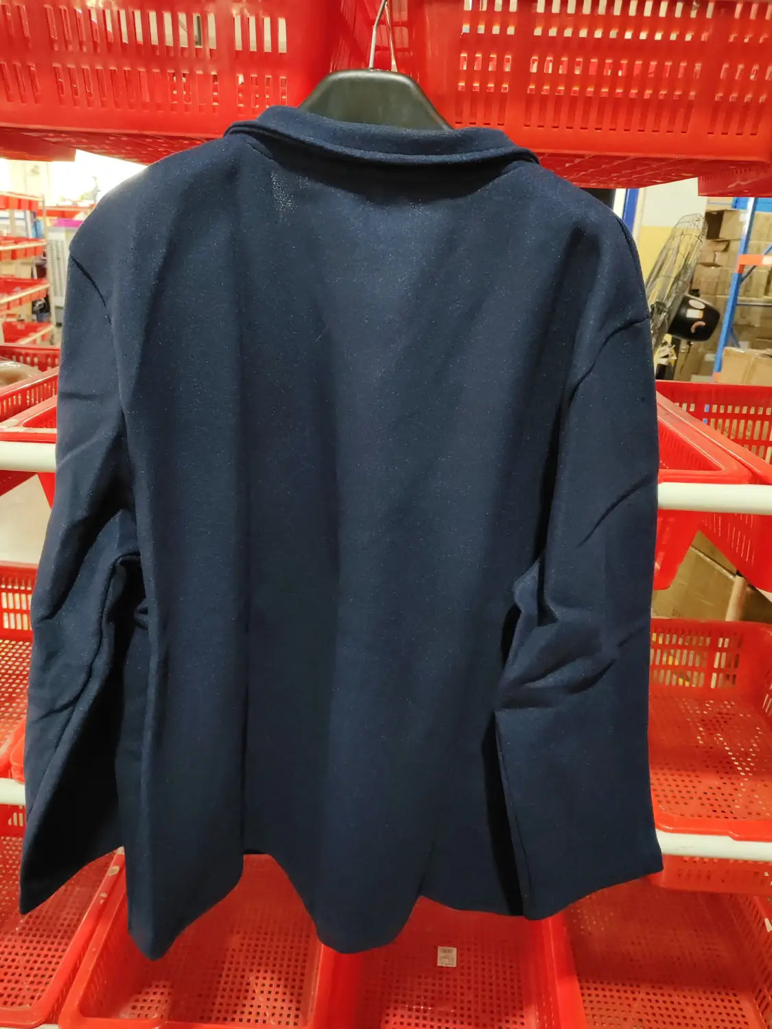 Navy blue wool men hip hop bomber jacket with a tailored fit and classic collar hanging on a black hanger against red plastic shopping baskets.