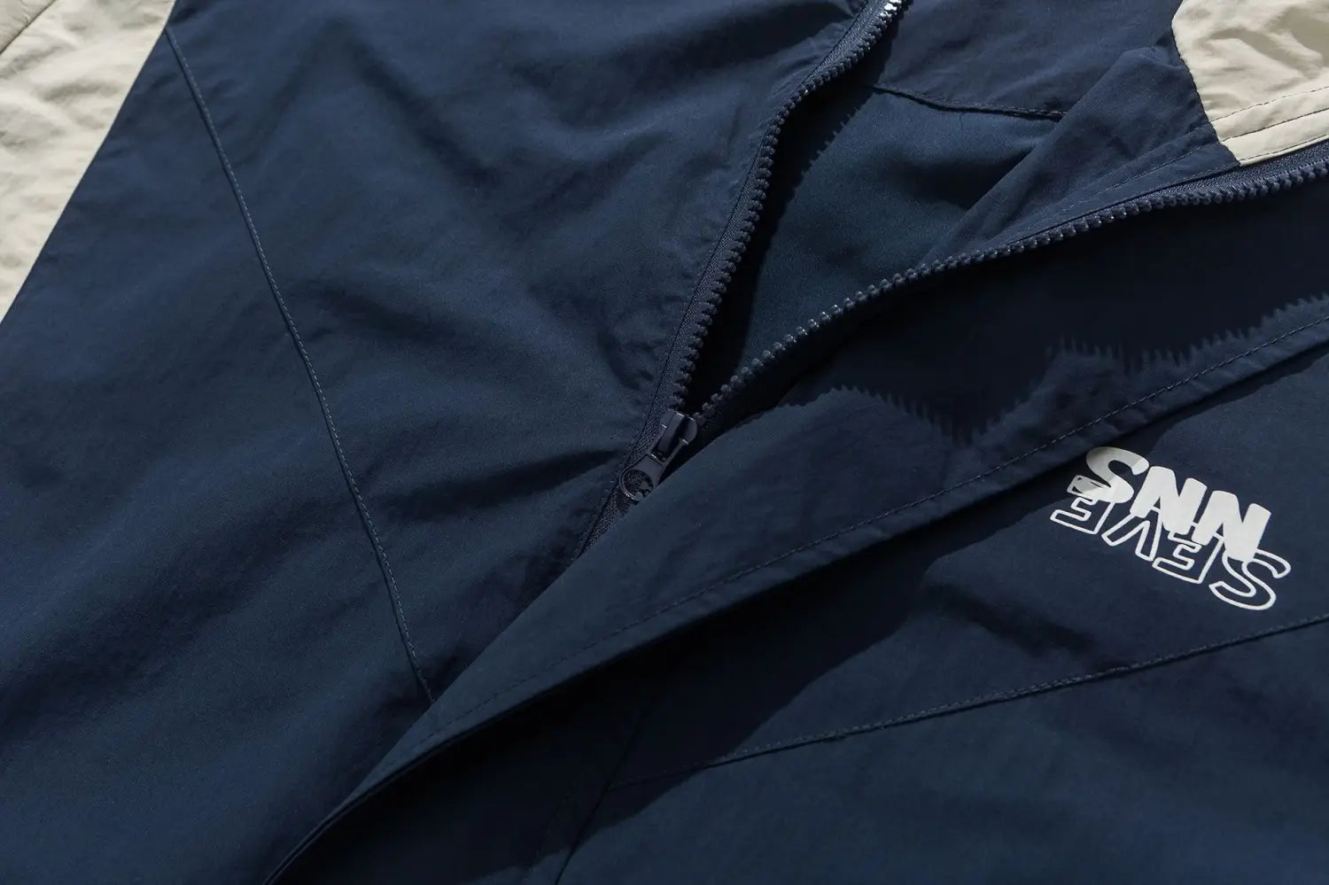 Veste coupe-vent ample à blocs de couleurs brodés en nylon bleu marine, avec un empiècement beige et un logo « snev » blanc.