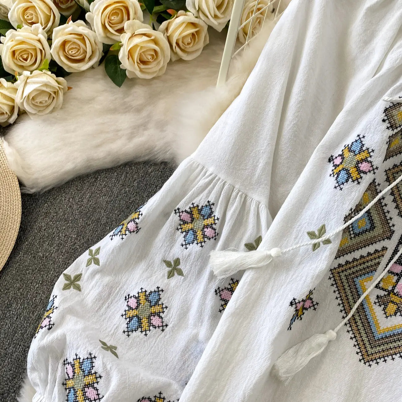 white embroidered lantern sleeve tie neck blouse featuring colorful embroidered patterns and tassels on a white fabric.