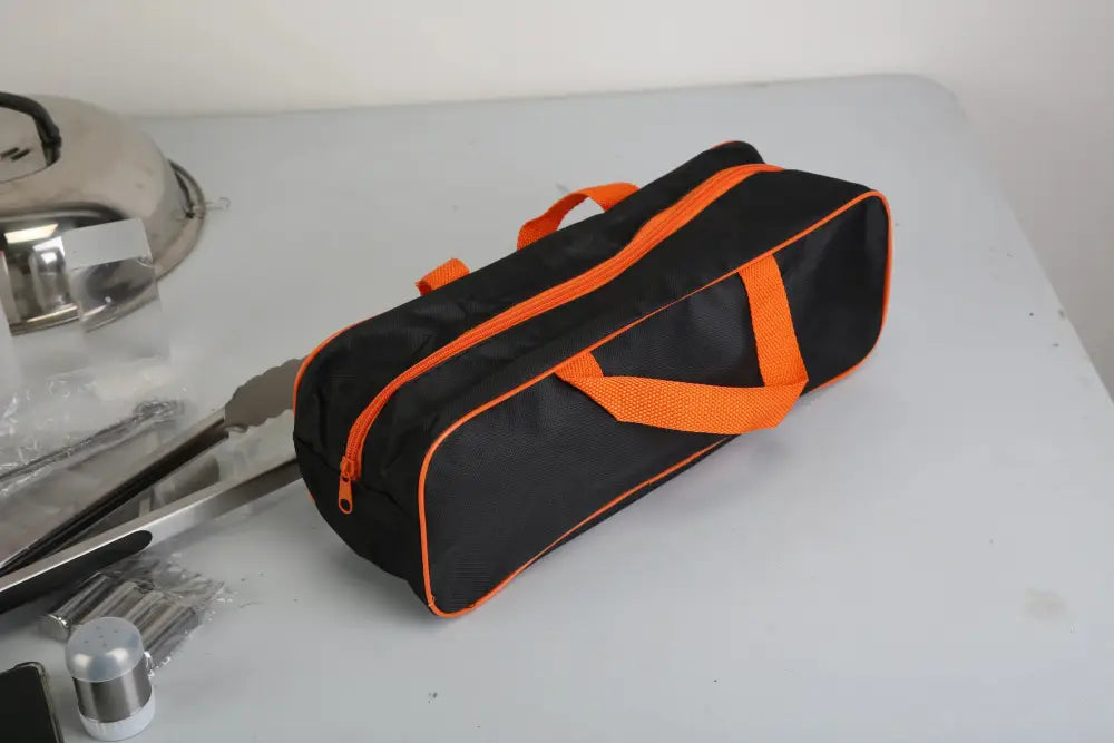 Black and orange tool bag with mesh side panel and zipper closure for 31 piece stainless steel flat top griddle accessory set