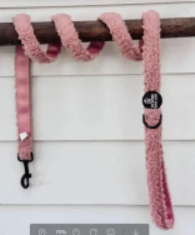 Correa para perro rosa y esponjosa de 1,5 m con herrajes negros de metal y un pequeño dije en forma de corazón blanco.
