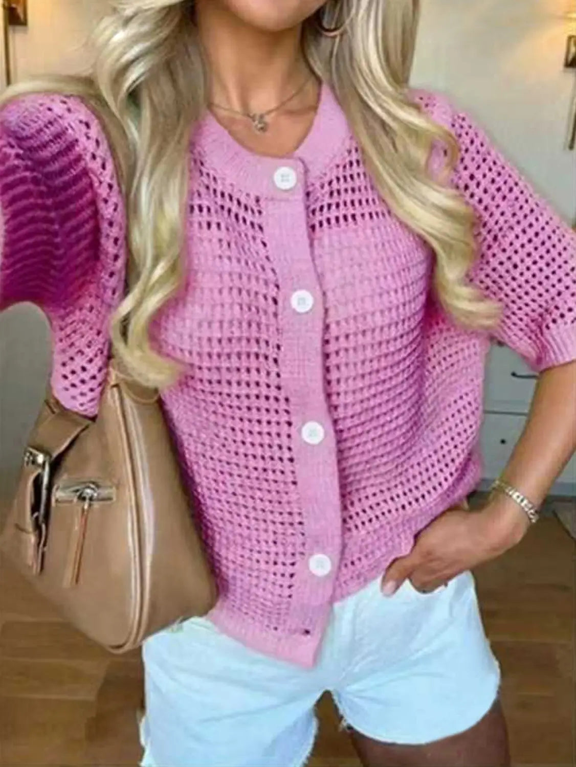 Un suéter tipo cárdigan de punto rosa con patrón de malla, botones blancos y mangas cortas, confeccionado con tejido de calado.