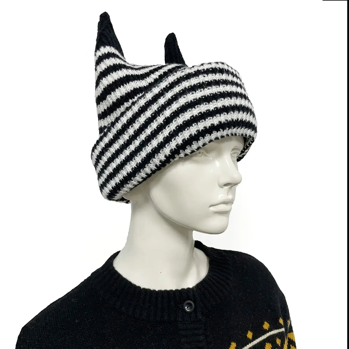 Bonnet hivernal de type cagoule tricoté à rayures noir et blanc, avec des protubérances pointues en forme de cornes, réalisé dans un fil souple.