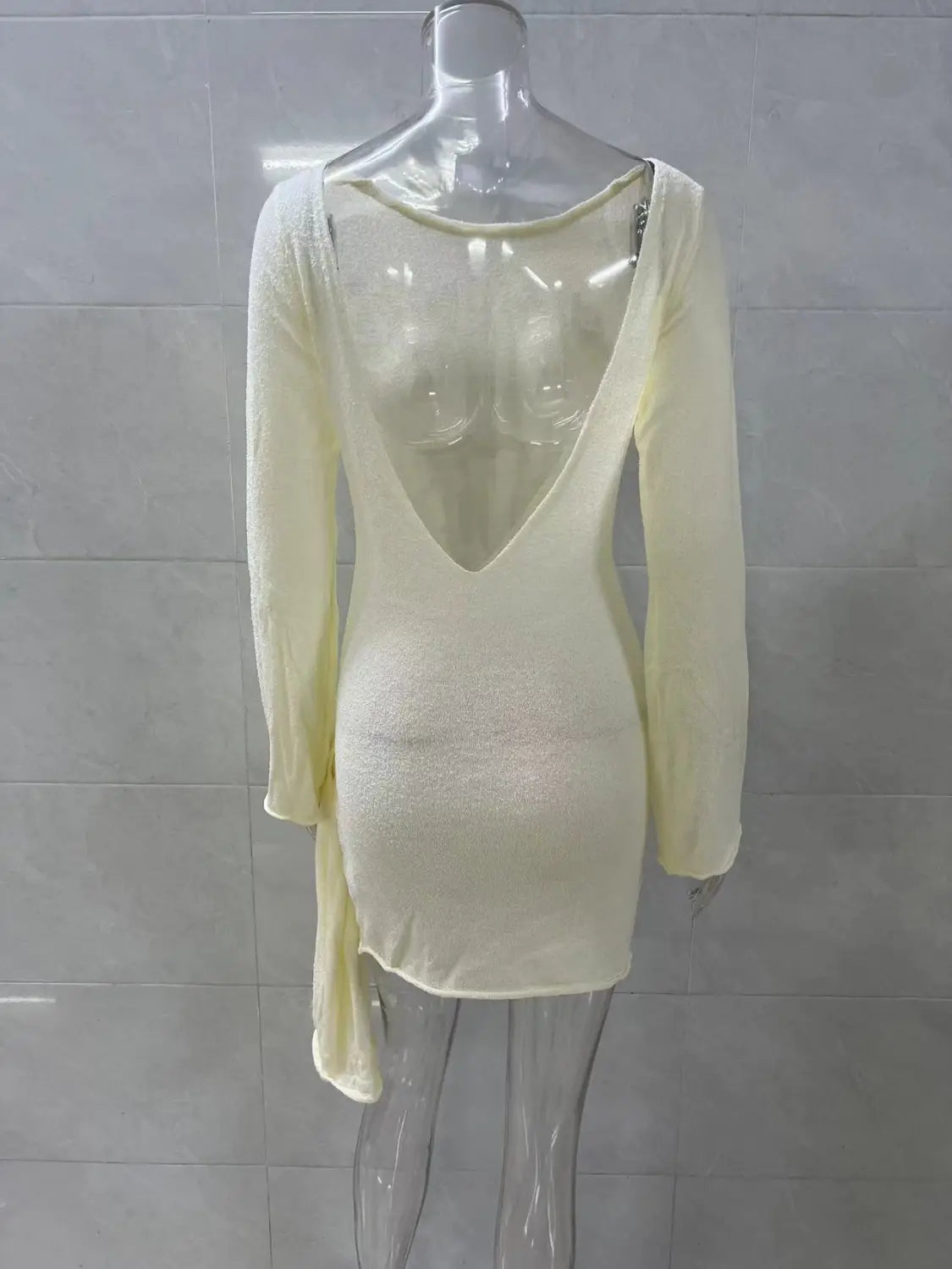 The back side of a creamy off-white long sleeve knit mini dress featuring a deep v-back and asymmetrical hemline with side tie detail.