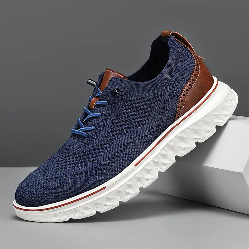 Navy blue men’s mesh knit casual lightweight sneaker with brown leather accents and a white rubber sole featuring red trim.