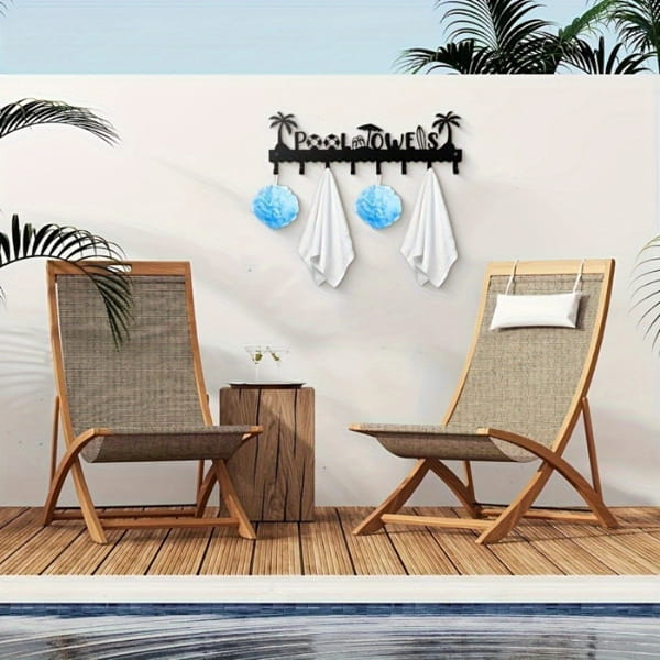 Black metal wall-mounted pool towel rack with eight hooks featuring palm tree and beach ball designs holding white towels and blue decorative balls.