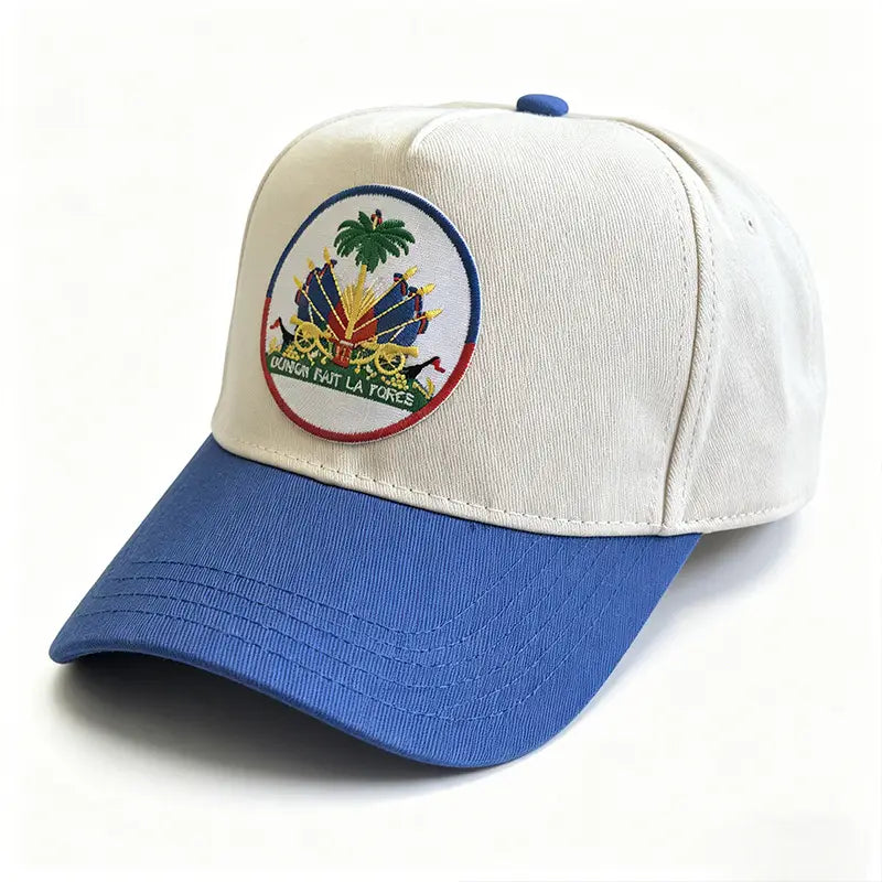 A two-tone baseball cap with a cream-colored crown and blue brim featuring an embroidered patch of the Haitian flag national emblem for sun protection.