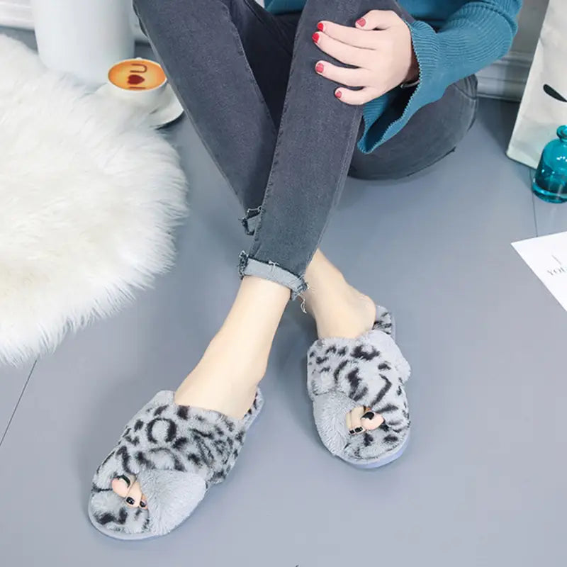 Gray fuzzy slip-on slippers with a leopard print pattern and small cat face embellishments designed as plush house slippers with cross straps.