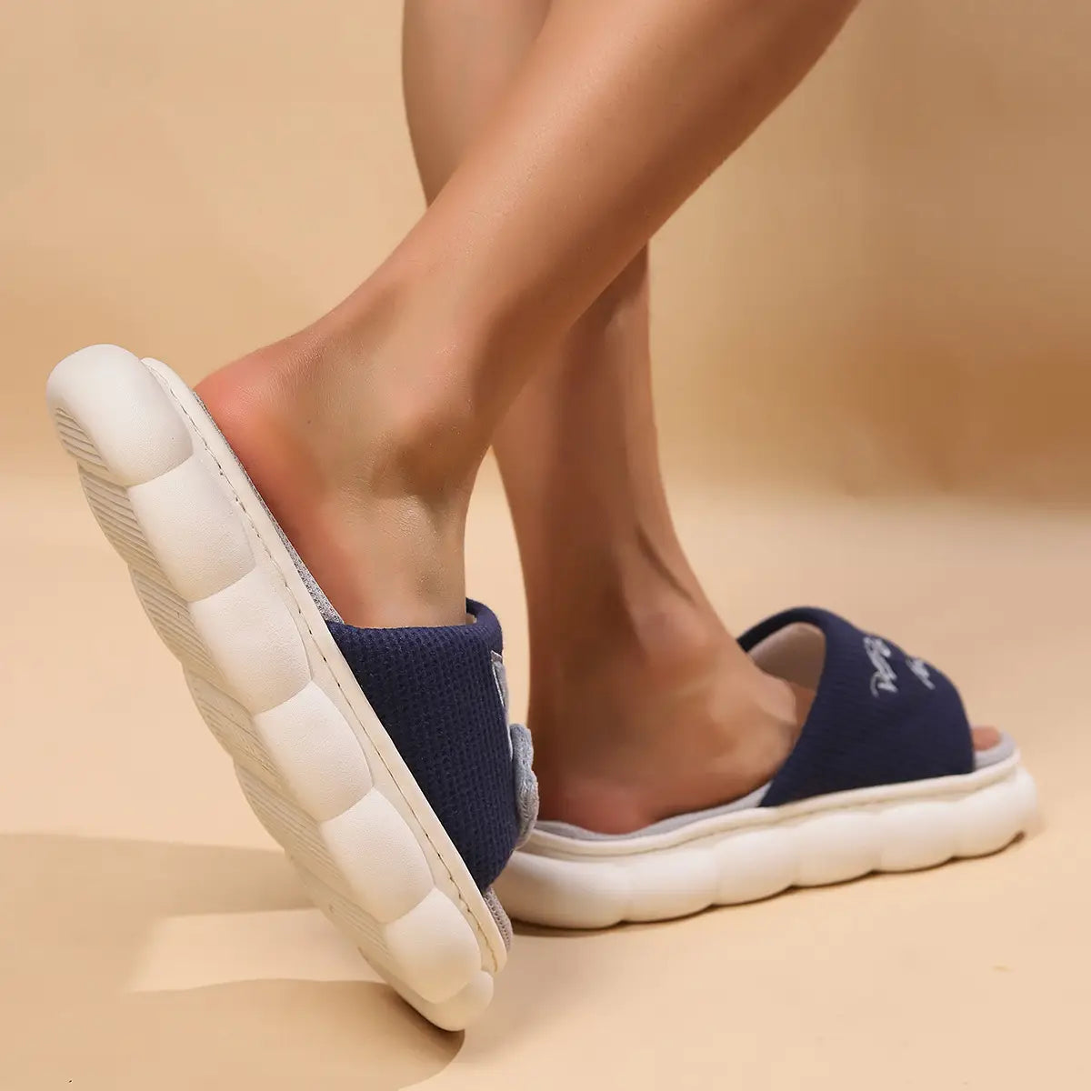 Navy blue knit slide sandals with a white rubber sole and embroidered cat cartoon detail designed as unisex anti slip slide slippers.