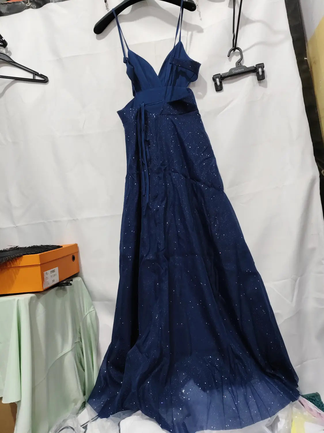 A navy blue shimmering v neck high slit maxi evening gown with thin spaghetti straps and subtle glittering embellishments throughout the fabric.
