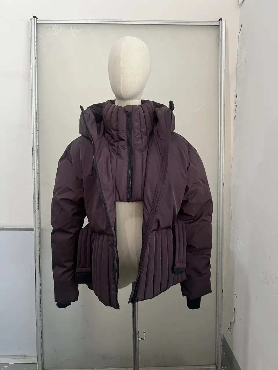 A plush dark purple belted hooded puffer coat for women featuring a high collar and pleated front panel.