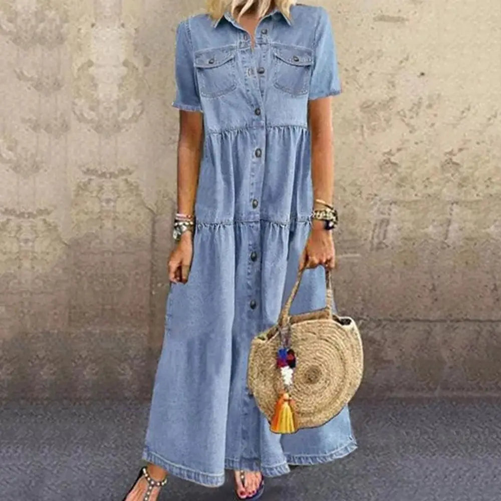 A light blue distressed denim maxi shirt dress featuring short sleeves, button-front closure, multi buckle accents, and tiered ruffles.