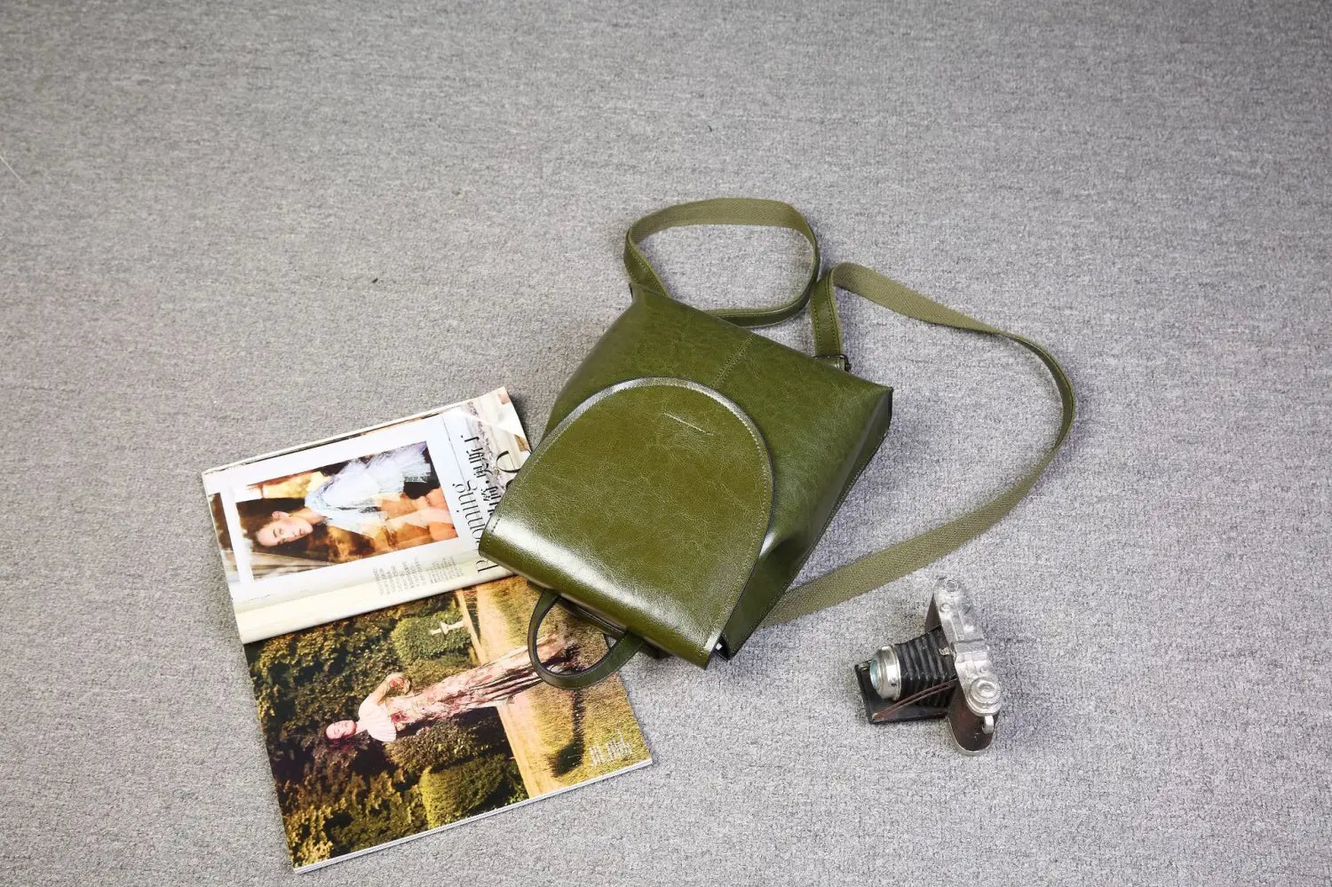 Mochila bandolera de cuero verde oliva con cierre de solapa curvada y correa de hombro ajustable, en diseño de moda retro.