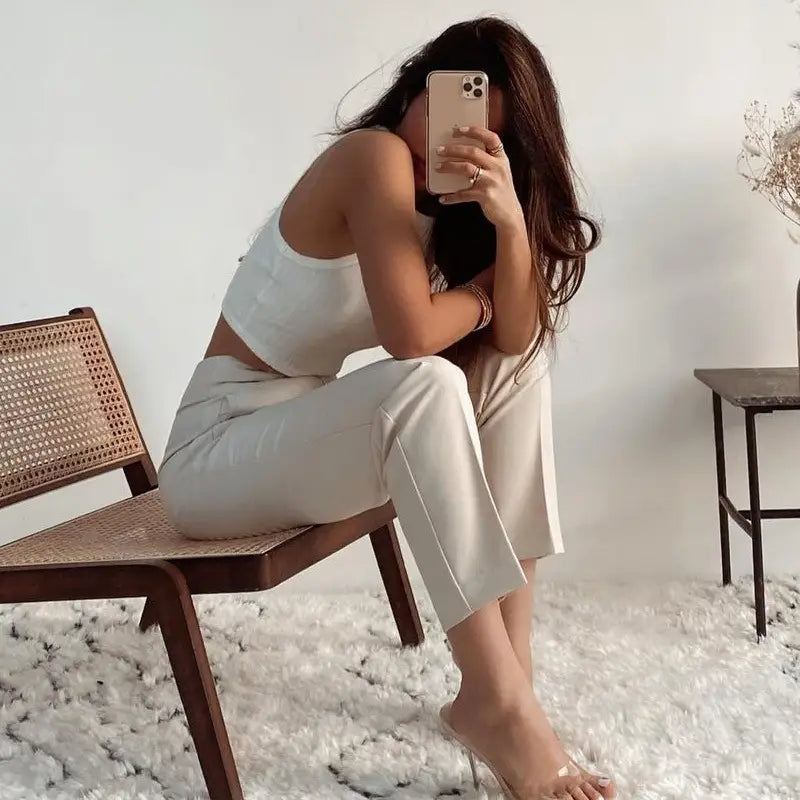 Une femme portant un pantalon taille haute à plis plats et jambes droites blanc, assise sur une chaise en canne tressée.