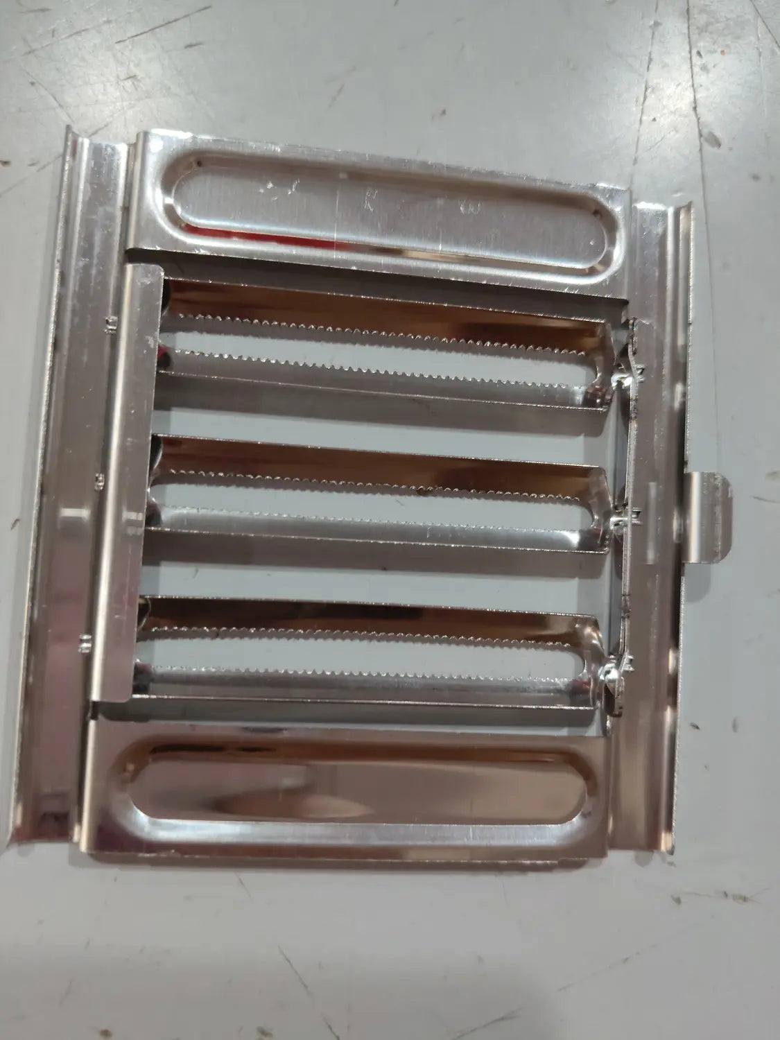 Juego de rallador y cortador multiusos metálico de acero inoxidable plateado con marco rectangular y múltiples cuchillas de molienda horizontales para una preparación eficiente de alimentos.