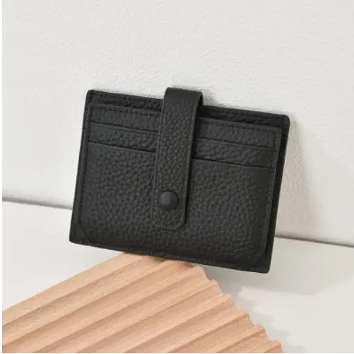 Black textured leather ultra thin minimalist card holder with flap closure secured by a single button and strap.