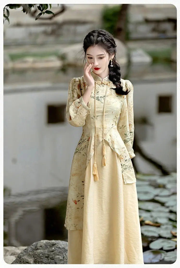 Une femme porte une robe cheongsam pêche brodée de fleurs, jaune pâle, à manches longues, avec des franges assorties à l’avant.
