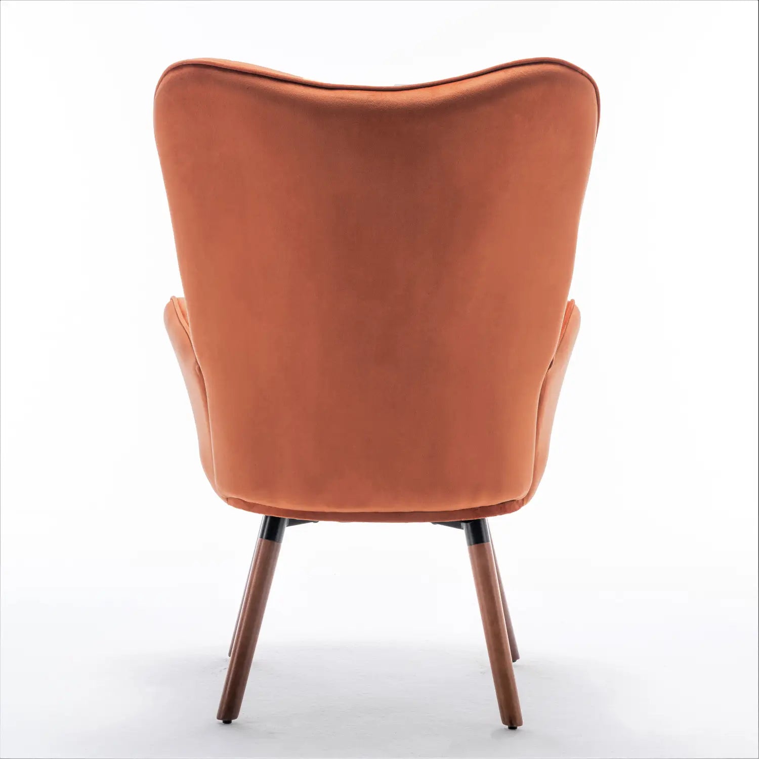 Una acogedora silla de acento tipo wingback de estilo moderno de mediados de siglo en terciopelo color óxido, con respaldo curvado y patas de madera.