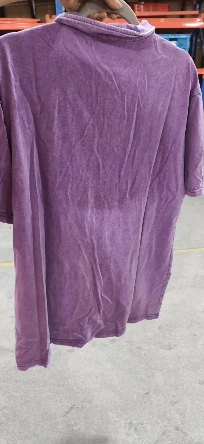 Lila ausgefranstes Baumwoll-Poloshirt mit langen Ärmeln und geripptem Rundhalsausschnitt, auf einem grauen Plastikhaken hängend.