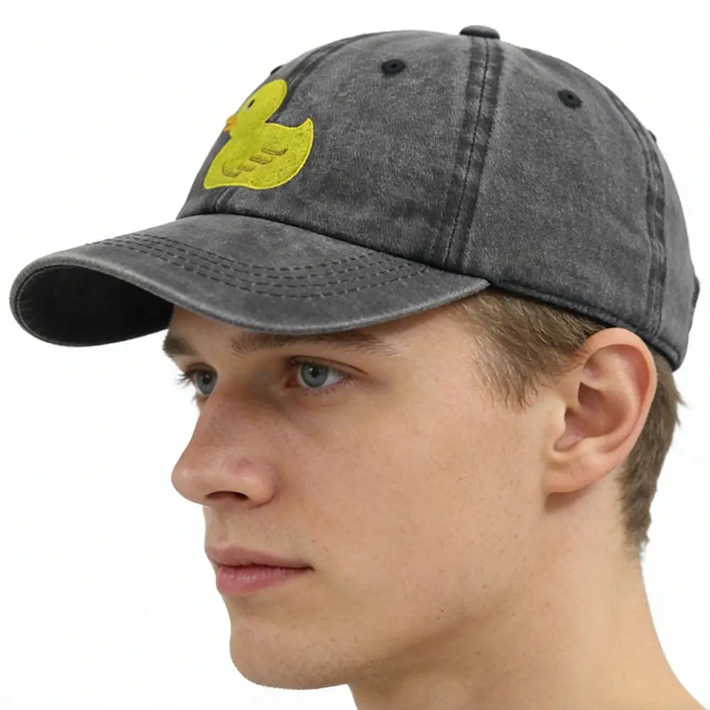 A faded gray distressed denim baseball cap featuring a bright yellow embroidered duck patch on the front.