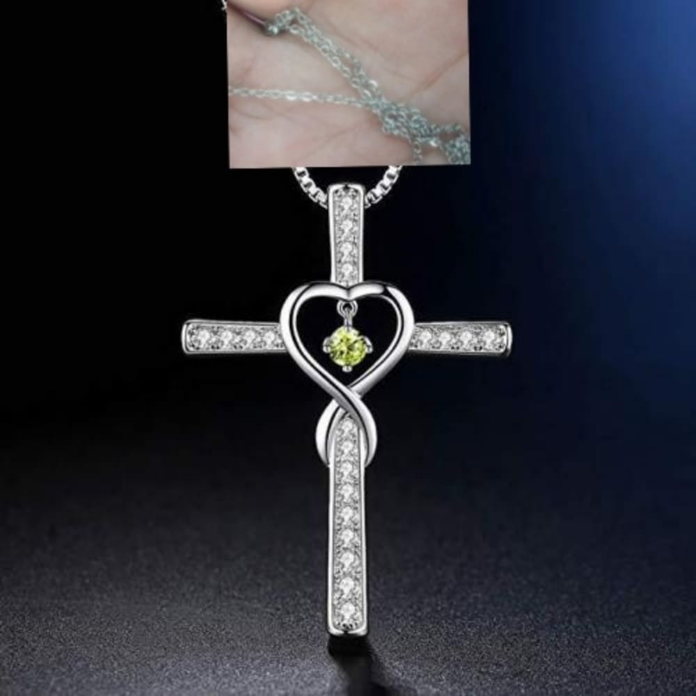 Silver cross pendant featuring a heart-shaped infinity knot design with clear cubic zirconia stones and a central green birthstone crystal in the infinity love heart cross birthstone crystal necklace.