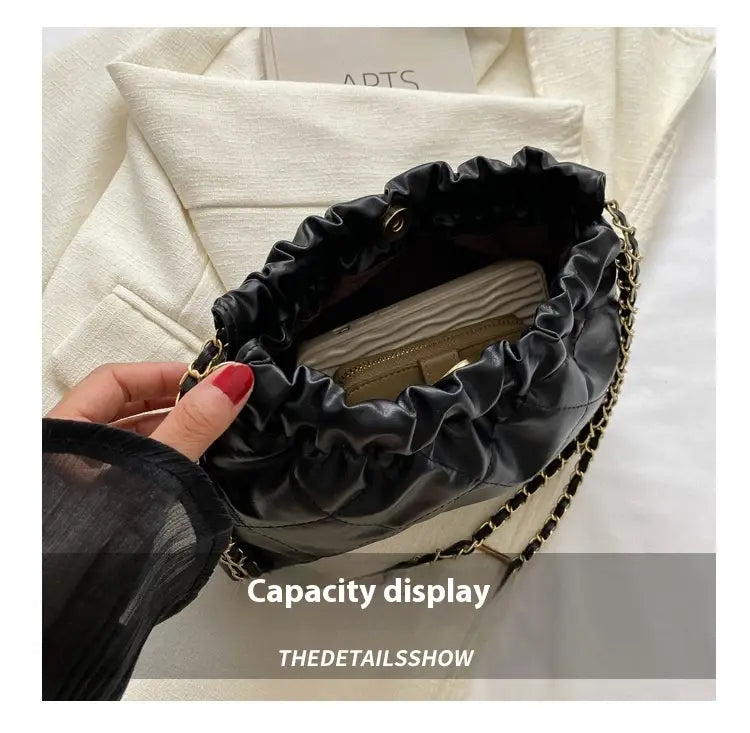 Black quilted faux leather crossbody bag with chain strap and ruffled top opening.