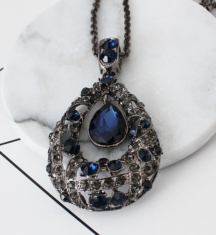 An ornate dark blue teardrop filigree pendant necklace with intricate silver-toned metalwork and sparkling rhinestones on a Korean style sweater chain.