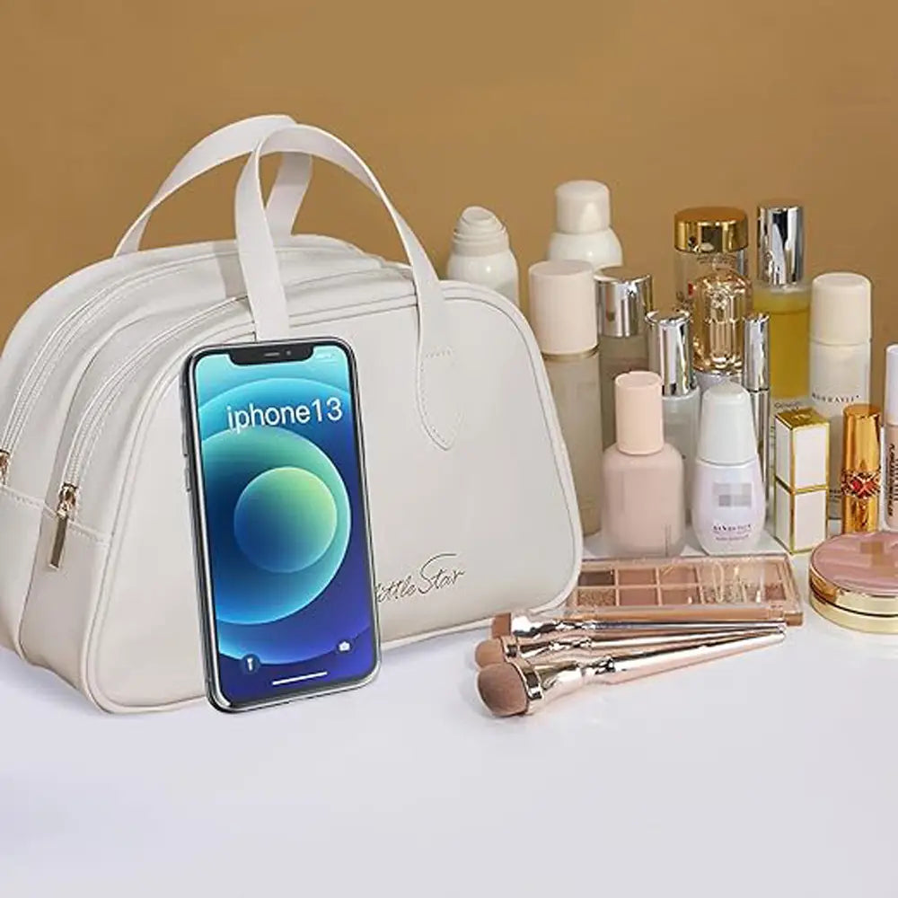 Une trousse de maquillage de voyage en cuir blanc, avec deux anses, des fermetures éclair de tonalité dorée et une broderie discrète du logo en forme de petite étoile, conçue comme une trousse de toilette imperméable.