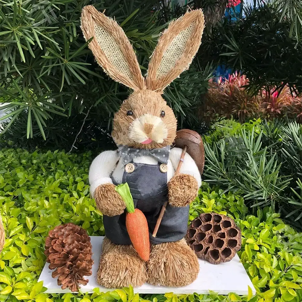 A 35cm rustic brown straw Easter rabbit figurine dressed in white shirt blue overalls holding an orange carrot