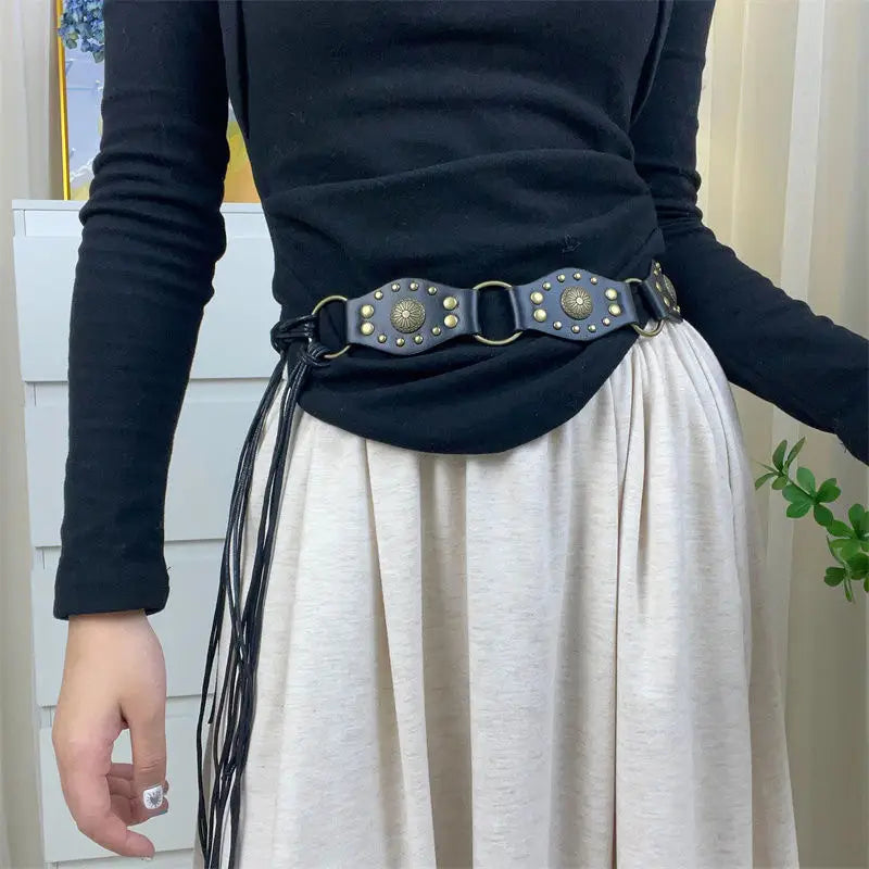 Dunkelgrauer Gothic-Punk-Lederharness-Gurt mit goldfarbenen kreisförmigen Nieten, Metallringen und einer geflochtenen Detail-Quaste aus schwarzem Band.