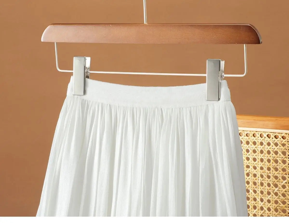 ein fließender weißer irrisierender Chiffon-Faltenrock, der an einem Holzkleiderbügel hängt