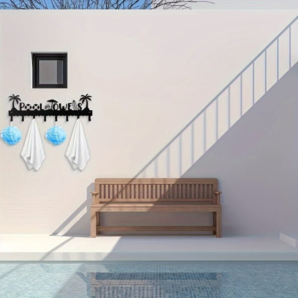 black metal pool towel rack wall mounted with 8 hooks featuring a palm tree design holding white towels and blue decorative items