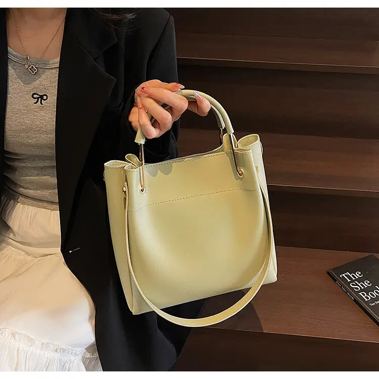 A pale yellow minimalist leather bucket bag with a top handle and detachable shoulder strap.