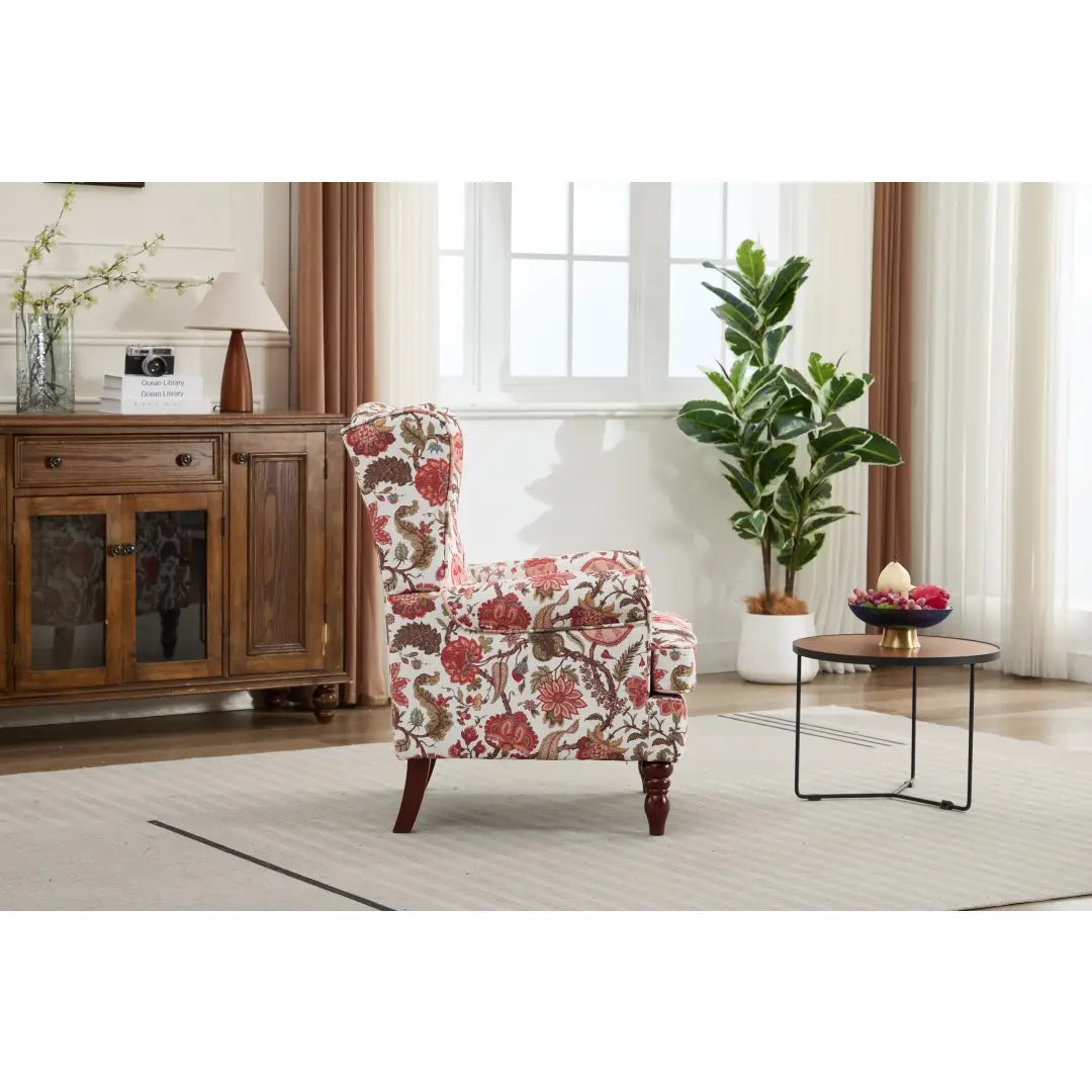 Una silla tipo ala con respaldo capitoné floral, tapizada en un tejido con flores rojas, marrones y crema sobre un fondo claro, con patas de madera retro.