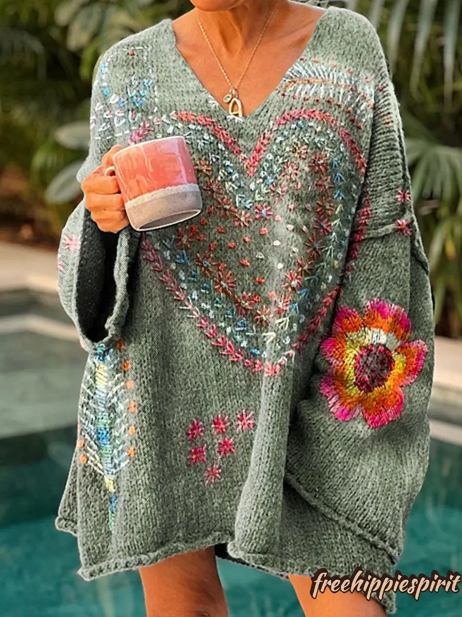 Un suéter de punto acogedor color verde oliva, confeccionado con material esponjoso y con bordados coloridos y vibrantes de un gran corazón y motivos florales, para vestir en Navidad.