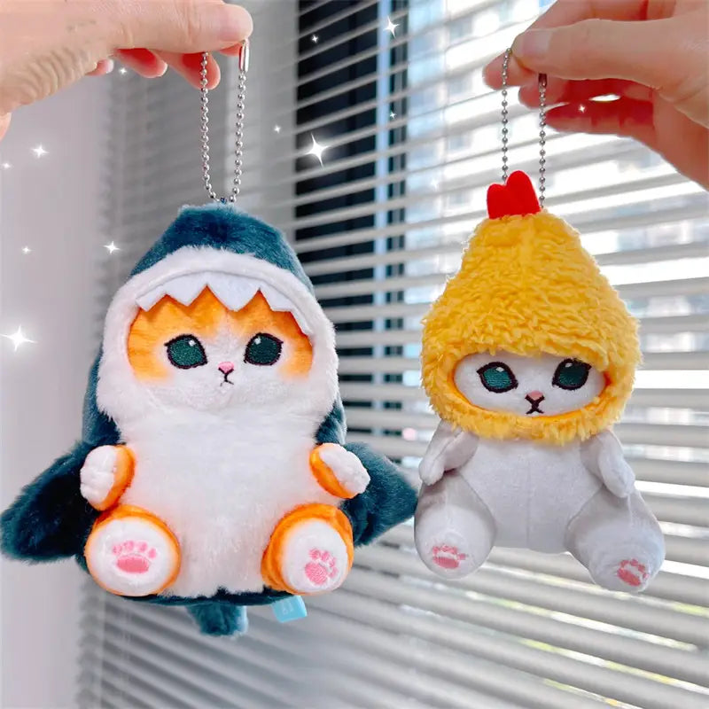 ティール色と白のサメのフードをかぶった猫（オレンジの差し色付き）と、ふわふわの黄色の鶏をテーマにした猫を、柔らかな生地で表現した「猫サメ」ぬいぐるみキーホルダー。