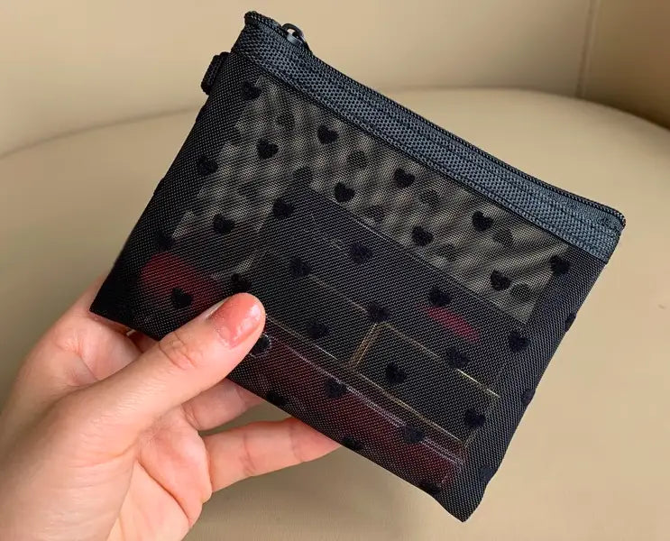 Eine schwarze Mesh-Kosmetiktasche mit einem schwarzen Herz-Punkte-Muster, herzförmigen Aussparungen und Reißverschluss.