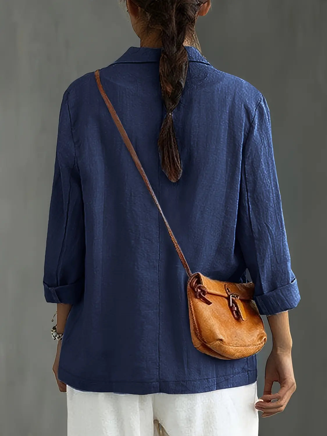 un bolso cruzado de cuero color camel con cierre simple de hebilla y correa a juego, combinado con un blazer de lino para mujer, casual y de trabajo.