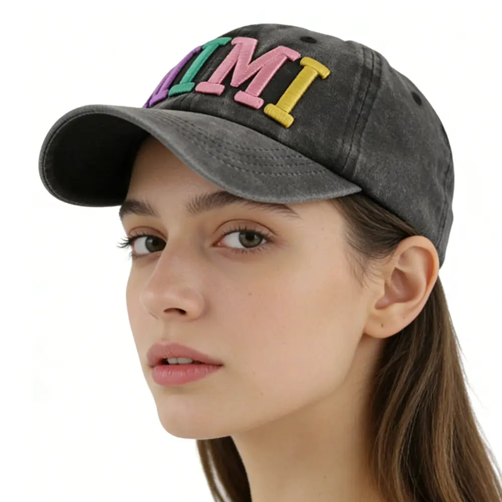 A faded black baseball cap featuring colorful embroidered letters spelling mi in pink green and yellow from the Rainbow Mimi Embroidered Baseball Cap collection.