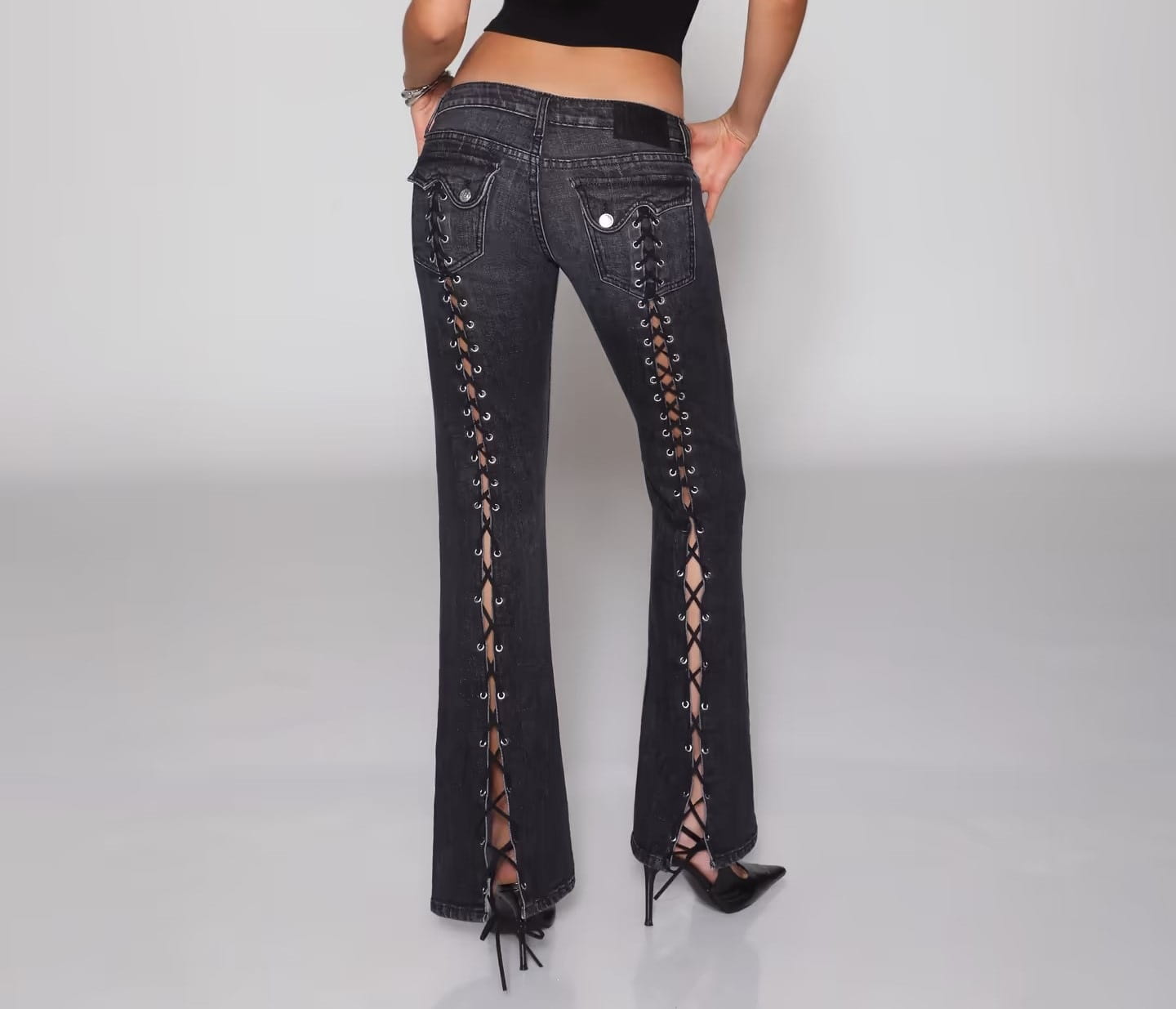 Jeans de mezclilla de tiro bajo tipo campana en negro con detalles de encaje con cordones a lo largo de las costuras exteriores, elaborados con material de mezclilla.